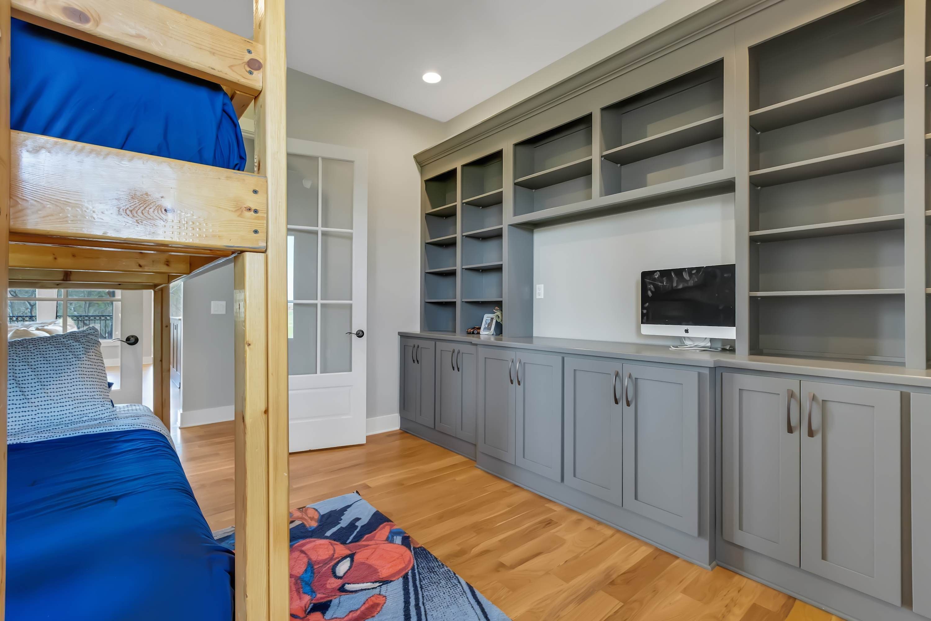 A bedroom with a bunk bed, grey cabinets, a television, and a window.