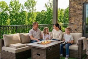 A family of four seated on a beige outdoor sofa with a fire feature in front. - Serene SC Getaway Firepit Sleeps 8 (West Union)