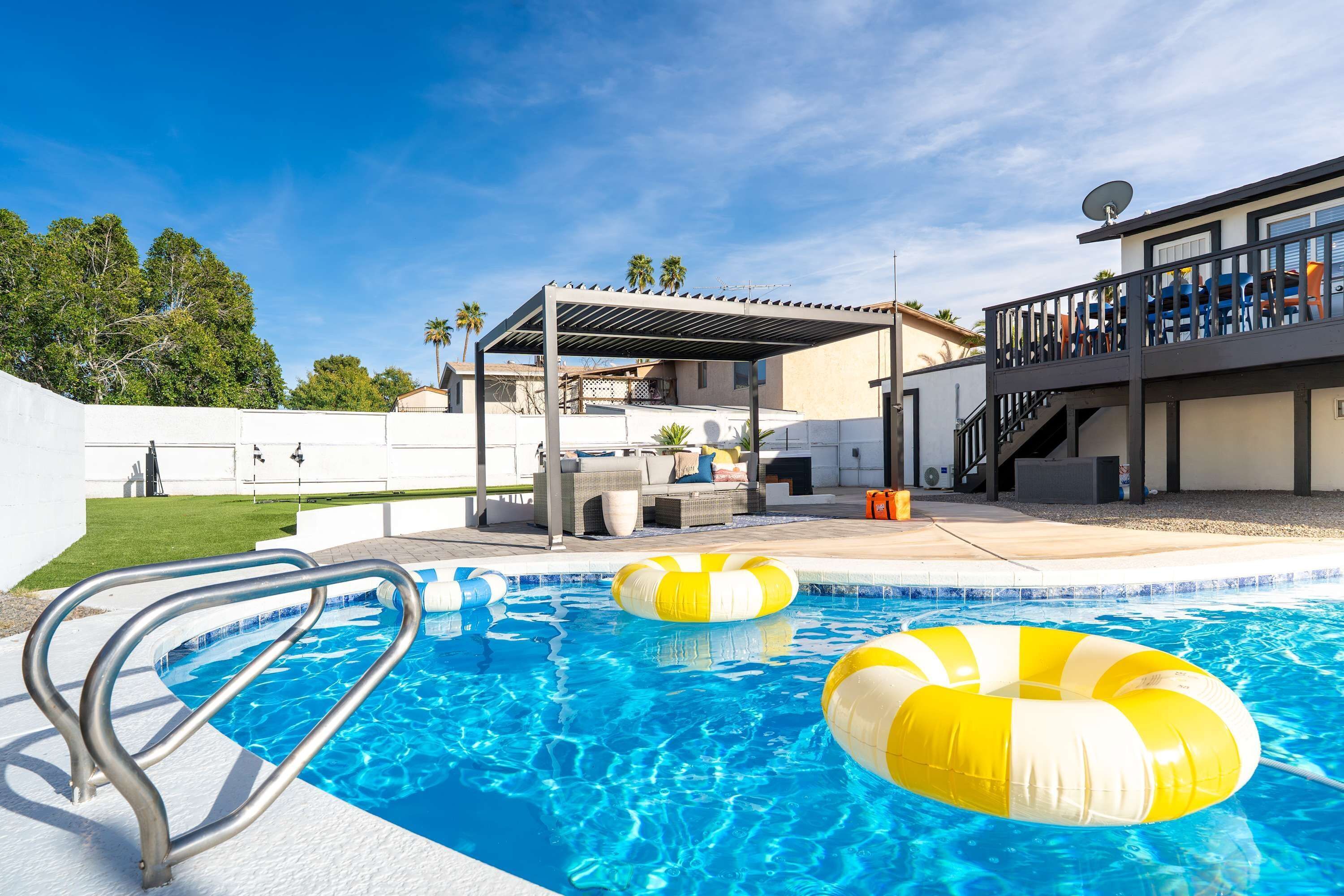 Piscina con terraza techada, sillas de descanso y vista a un edificio residencial.
