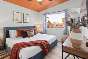 A bedroom with a bed, pillows, a nightstand, a lamp, a window with curtains, a hanging light fixture, and a vase with dried flowers. - Piece of Paradise Pool Games Fire Pit Hot tub (Glendale)