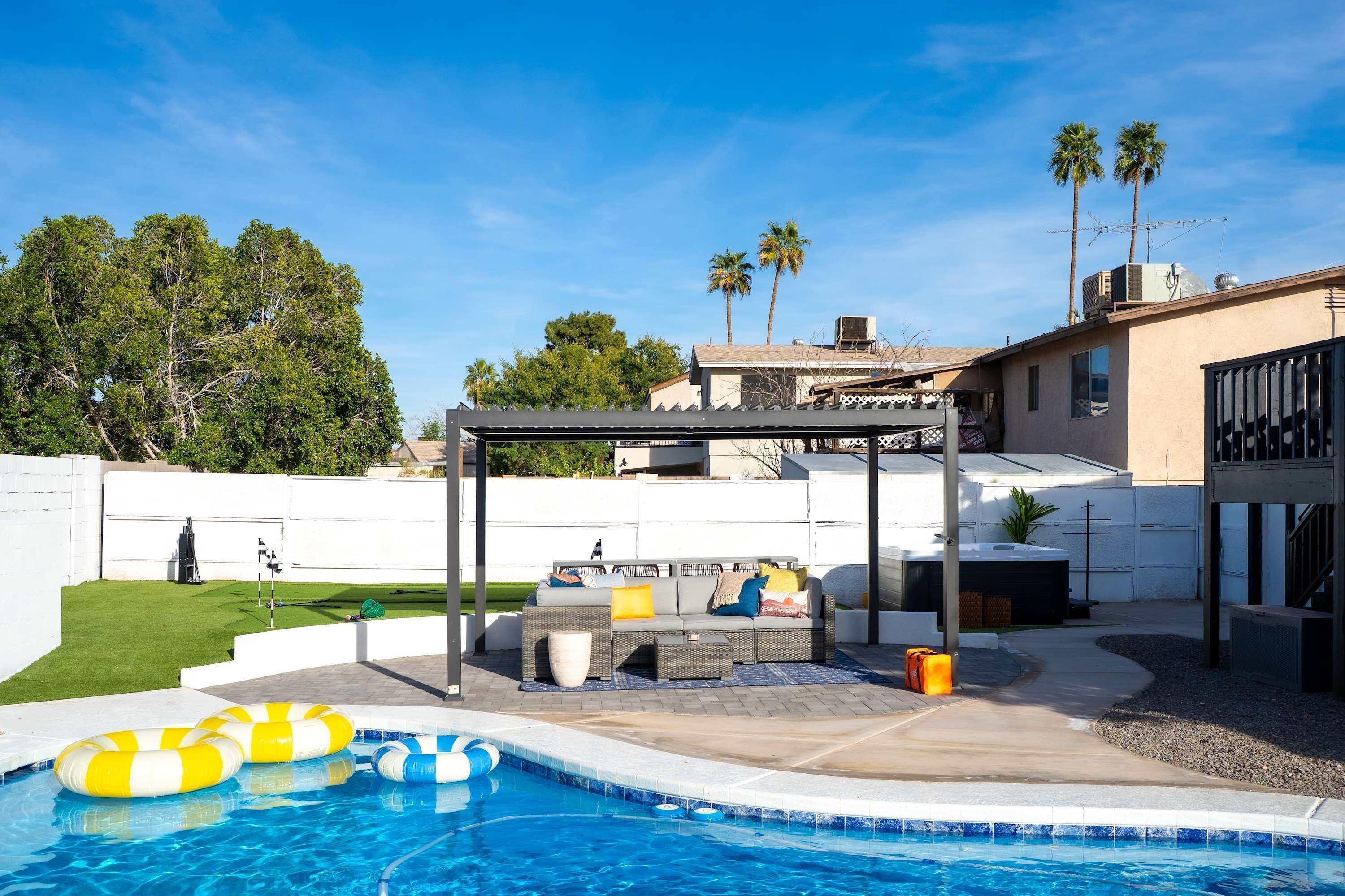 A backyard with a swimming pool, outdoor seating, and palm trees.