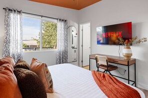 A hotel room with a bed, a desk, a television displaying the Netflix logo, and a window with curtains. - Piece of Paradise Pool Games Fire Pit Hot tub (Glendale)