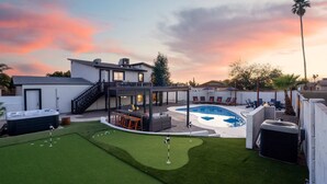 Een achtertuin met zwembad, hottub en overdekt terras.