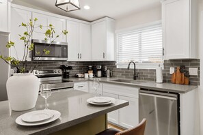A modern kitchen with white cabinets, stainless steel appliances, a granite countertop, and a window with blinds. - Piece of Paradise Pool Games Fire Pit Hot tub (Glendale)
