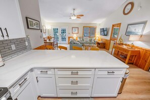 Une cuisine moderne avec des meubles blancs, un îlot central et un coin repas doté de chaises en bois.