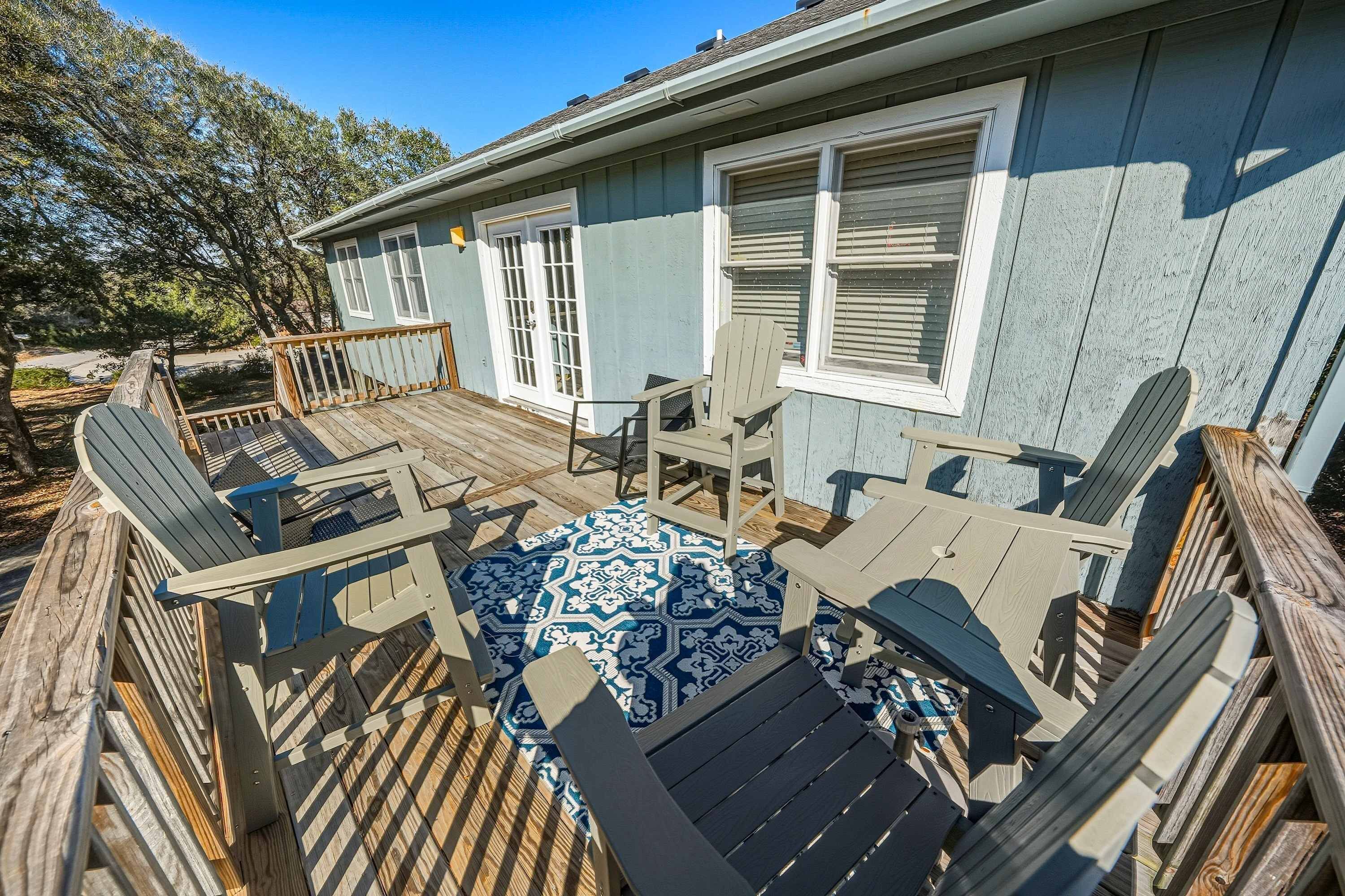 A deck with outdoor furniture, a patterned rug, and a house with a blue exterior and white trim.