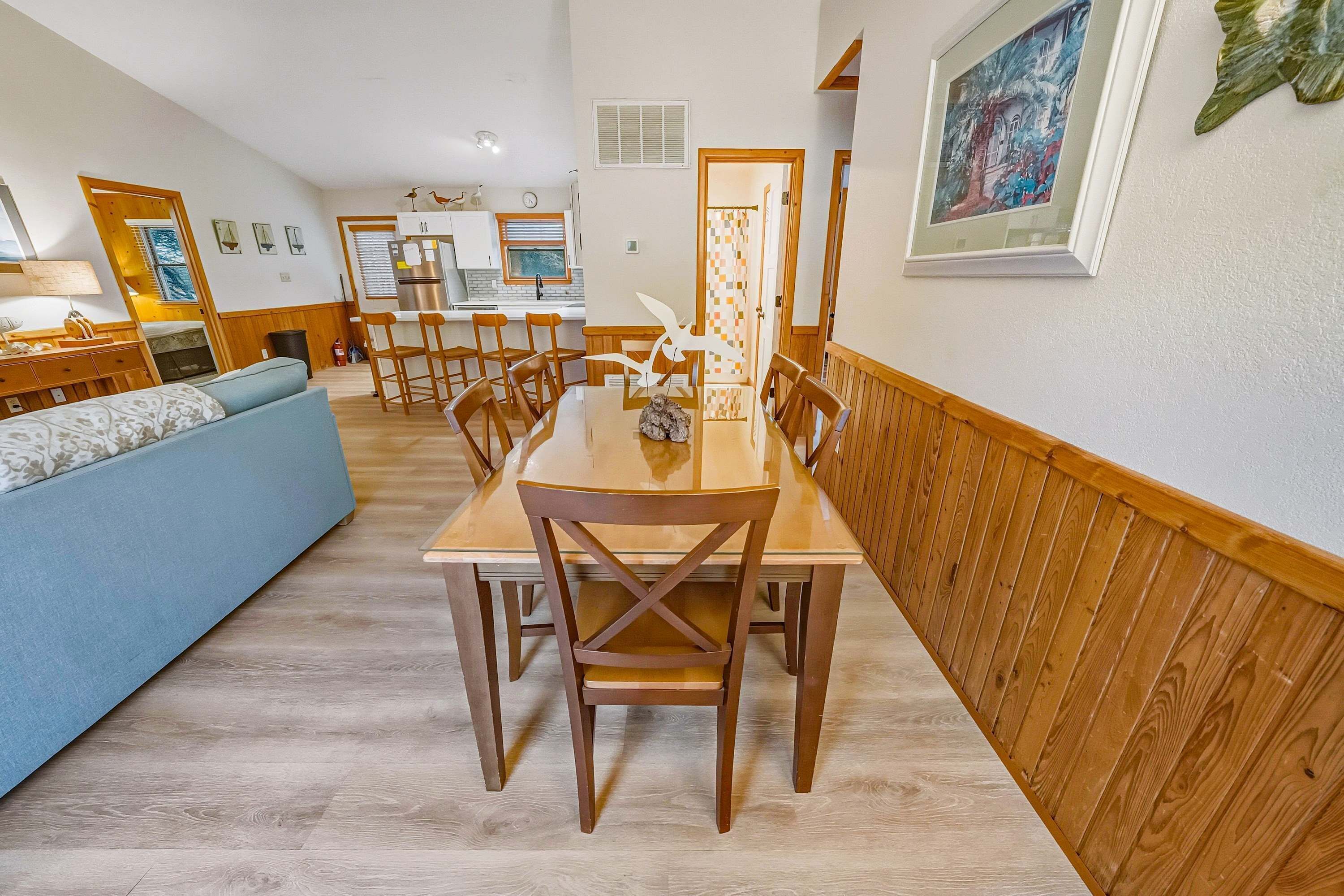 A dining area with a wooden table and chairs, a blue sofa, and a kitchen in the background.