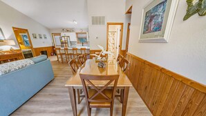 Un comedor con una mesa y sillas de madera, un sofá azul y una cocina al fondo.