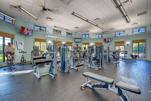 Une salle de sport équipée de divers appareils d’exercice, dotée de grandes fenêtres et affichant une enseigne pour Lennar Homes.