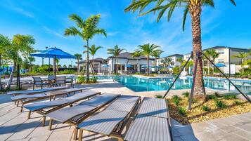 A poolside area with lounge chairs, umbrellas, and palm trees.