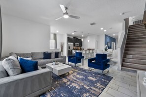 Una sala de estar moderna con un sofá gris, sillas azules, una mesa de centro blanca y una alfombra estampada.