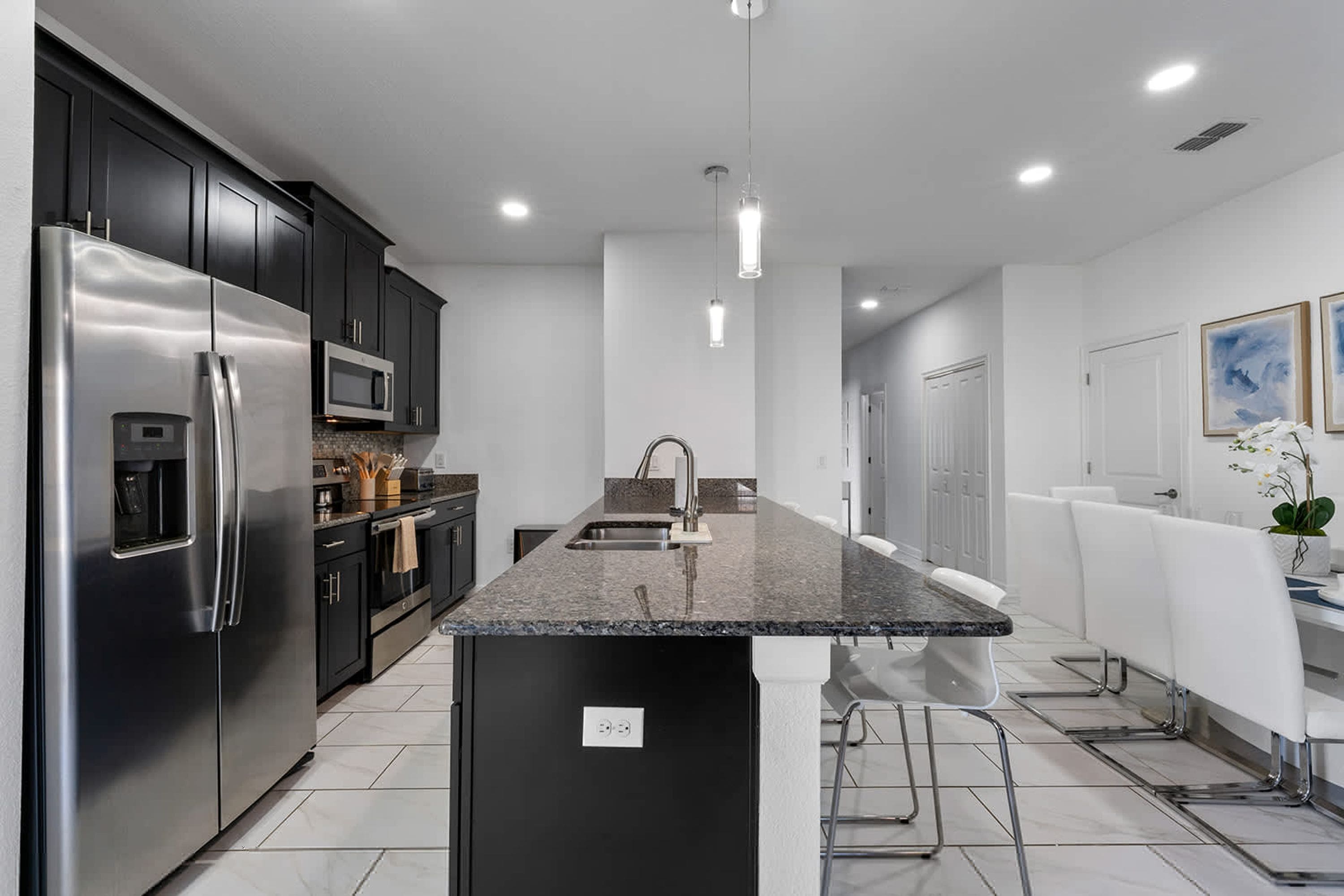 A modern kitchen with stainless steel appliances, a central island, and a dining area with white chairs.