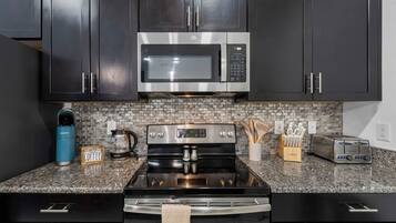 A modern kitchen with dark cabinets, a stainless steel microwave, a gas stove, and a toaster.