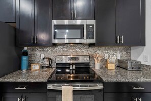 Una cocina moderna con armarios oscuros, un microondas de acero inoxidable, una estufa a gas y un tostador.