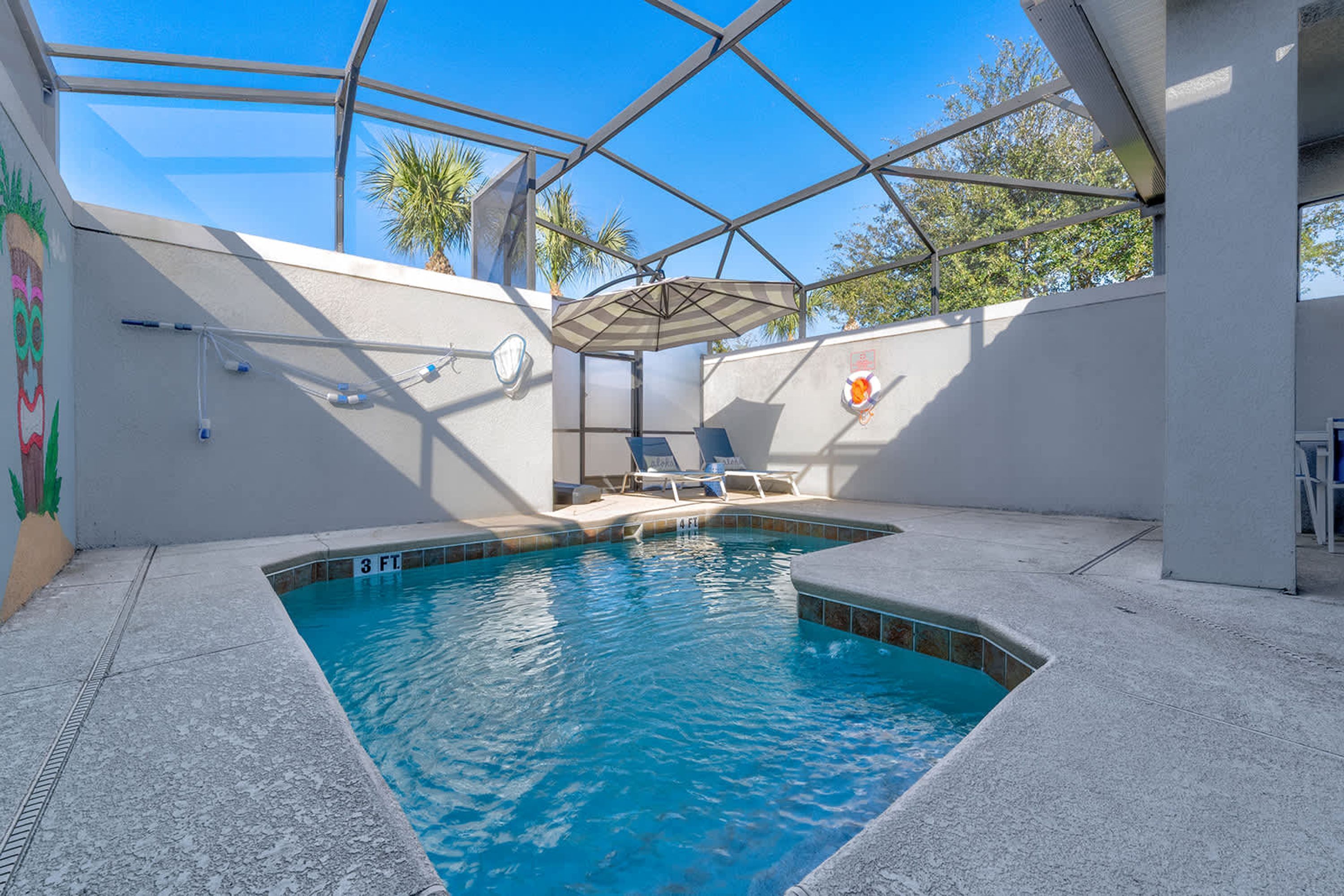 A swimming pool with a glass enclosure, lounge chairs, and a lifebuoy on the wall.