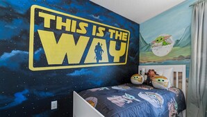 Ein Schlafzimmer mit Wandmalerei zum Thema Star Wars, einem Bett mit Bettwäsche mit Galaxie-Motiv und einer Steckdose.