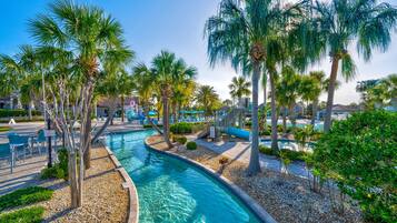 A pool area with clear water, surrounded by palm trees and a pebble-lined walkway.