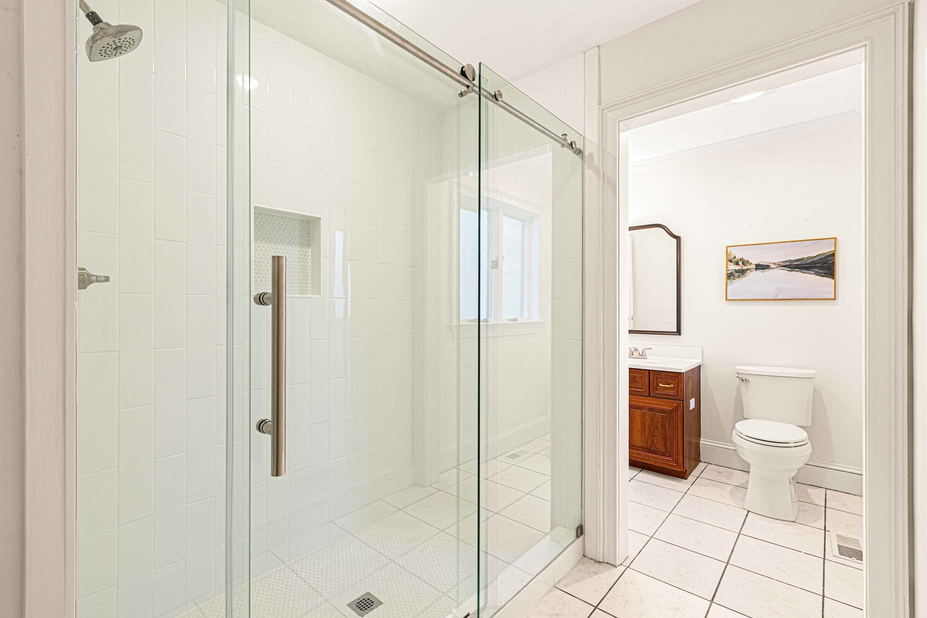A modern bathroom with a glass shower enclosure, a toilet, and a sink with a wooden cabinet.