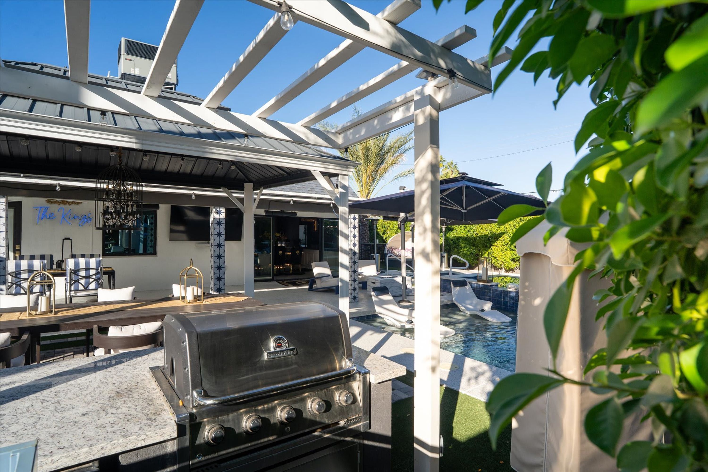 Un espace aménagé au bord de la piscine, comprenant un barbecue, des chaises longues et un coin salon abrité.