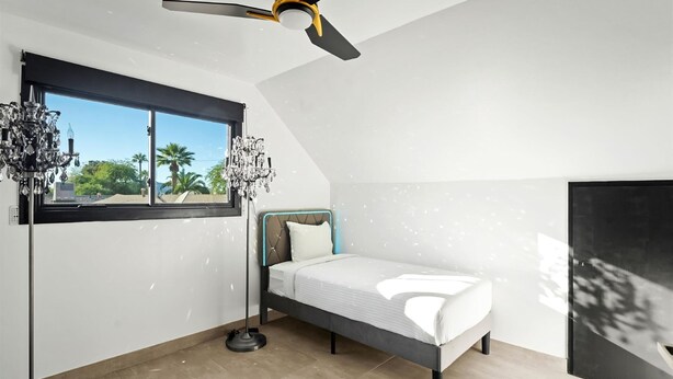 A bedroom with a bed, a standing lamp, a ceiling fan, and a window with a view of palm trees. - Luminosity Escape Pool Hot Tub Dog-friendly (Scottsdale)