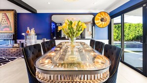 A modern dining area with a glass table surrounded by upholstered chairs, a vase with flowers, and a large decorative light fixture. - Luminosity Escape Pool Hot Tub Dog-friendly (Scottsdale)
