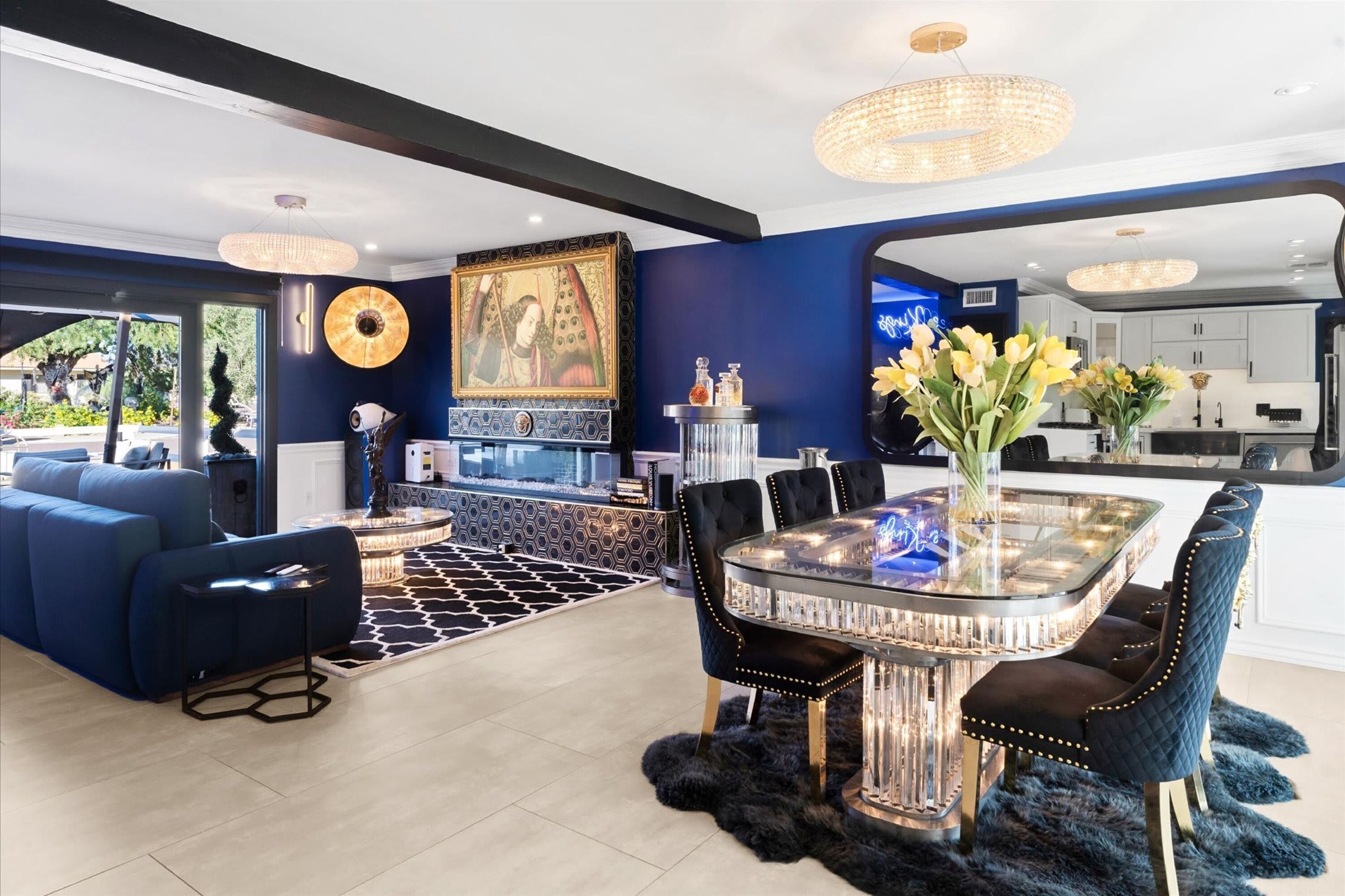 A modern interior with a dining area, sofas, a chandelier, and a large painting.