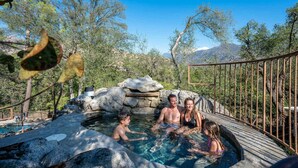 A hot spring with a wooden deck, surrounded by trees and a mountainous backdrop. - Prime Sequoia Stay Pool Hot Tub Sauna Views (Three Rivers)