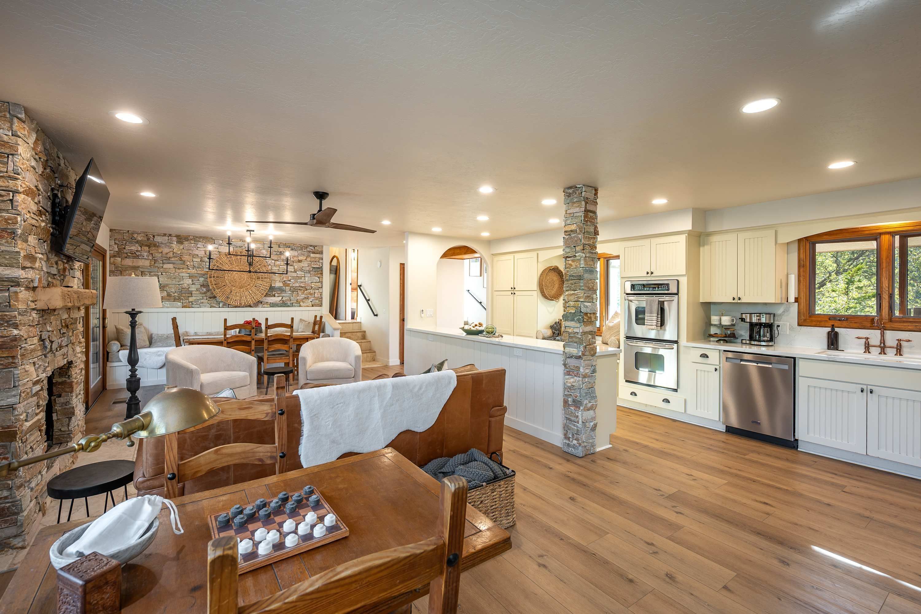 A spacious living area with a fireplace, a dining table with chairs, a kitchen with white cabinets, and a stone accent wall.
