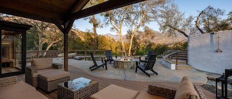 Une terrasse extérieure aménagée avec des meubles en osier, un foyer et une vue sur un paysage montagneux.