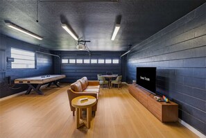 Een kamer met een pooltafel, een bank, een televisie en een plafondprojector.