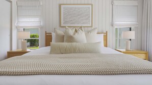 A neatly arranged bedroom with a large bed, two bedside tables with lamps, a framed artwork above the bed, and a window with a view of greenery. - Minutes to AMI Pool Game Room Sleeps 11 (Bradenton)