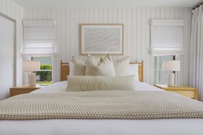 A neatly arranged bedroom with a large bed, two bedside tables with lamps, a framed artwork above the bed, and a window with a view of greenery. - Minutes to AMI Pool Game Room Sleeps 11 (Bradenton)