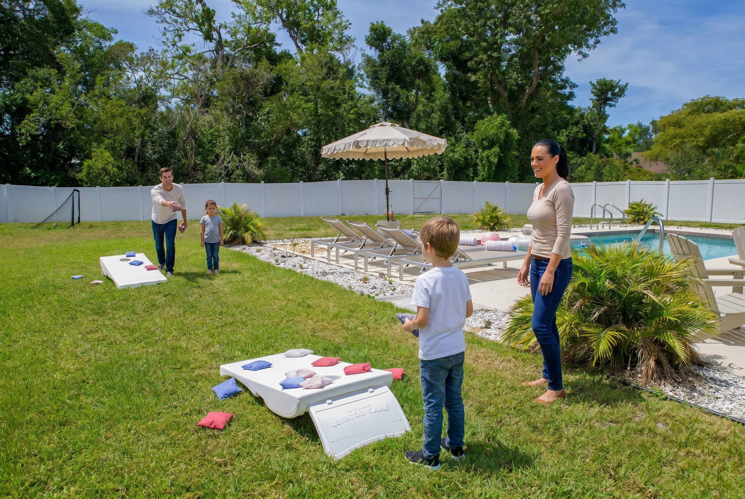 A backyard with a pool, a white fence, and a table with cushions.