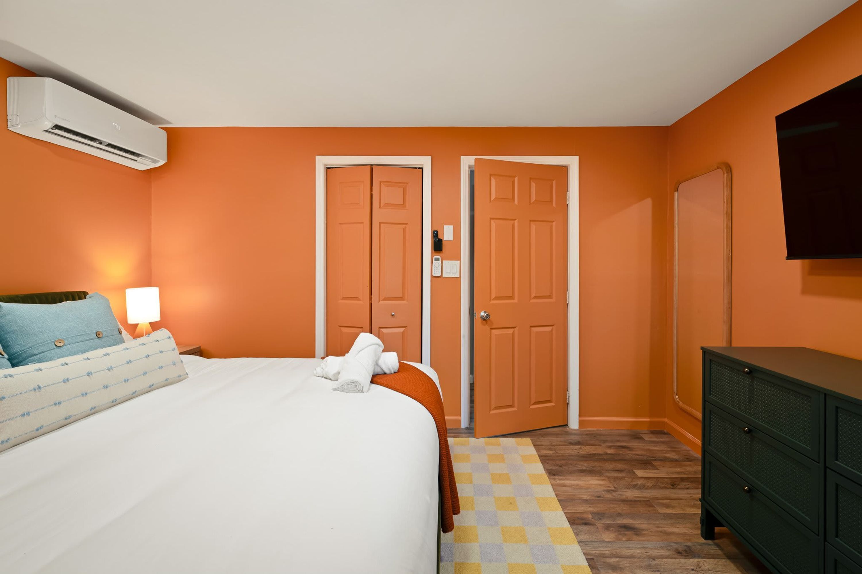A hotel room with a bed, a dresser, an air conditioning unit, and two doors.