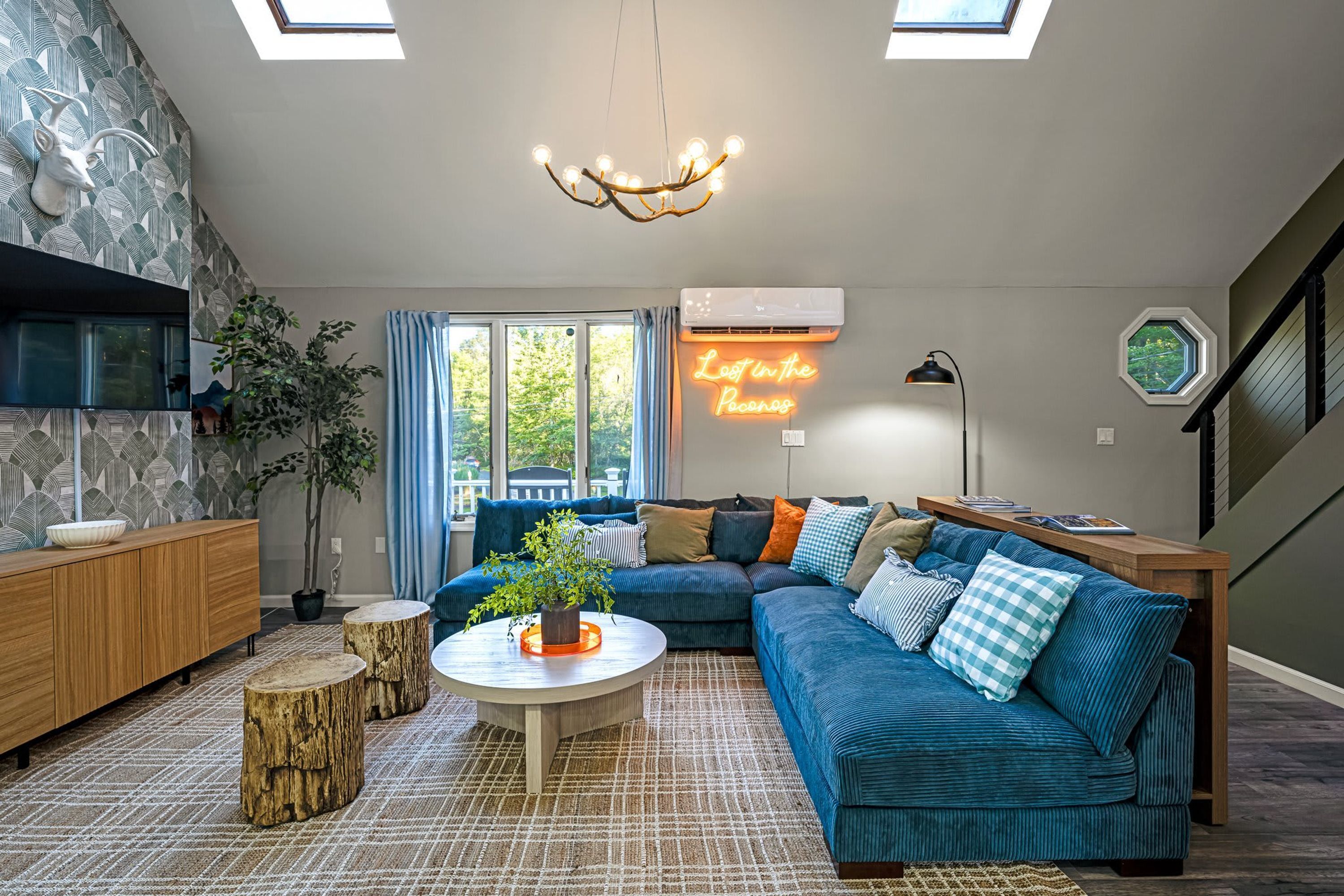 Un salon moderne avec un canapé d’angle, une table basse ronde et un panneau lumineux au néon.