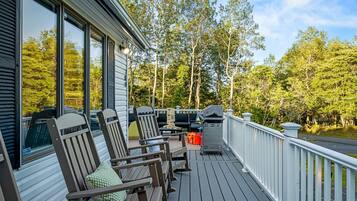A deck with outdoor furniture, a grill, and a view of trees.