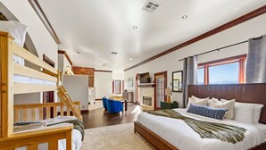 Une chambre avec un lit superposé, un grand lit avec de nombreux oreillers, un téléviseur à écran plat et une vue sur l’extérieur.