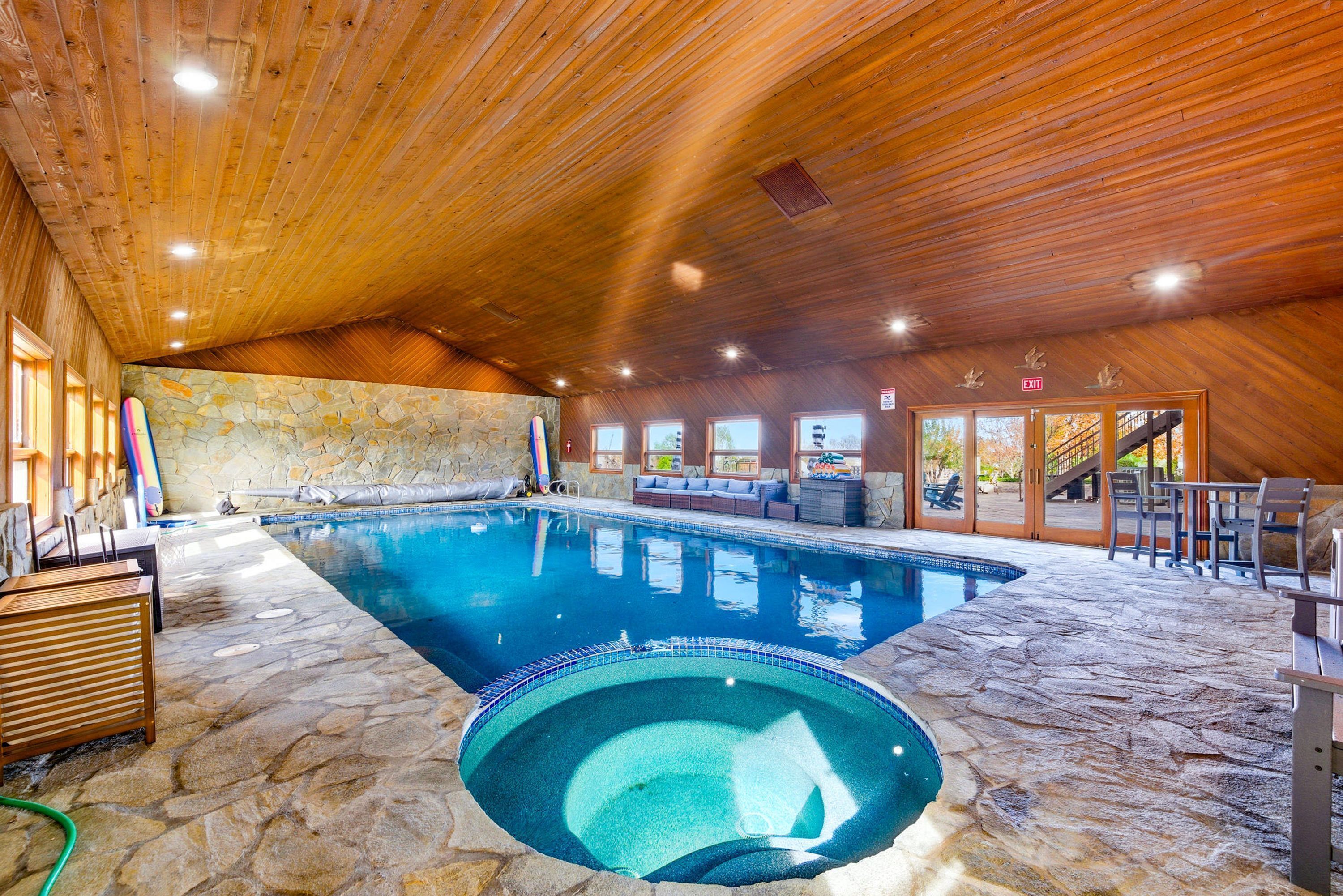 Una piscina interior con suelo de piedra, techo de madera y zonas de estar.