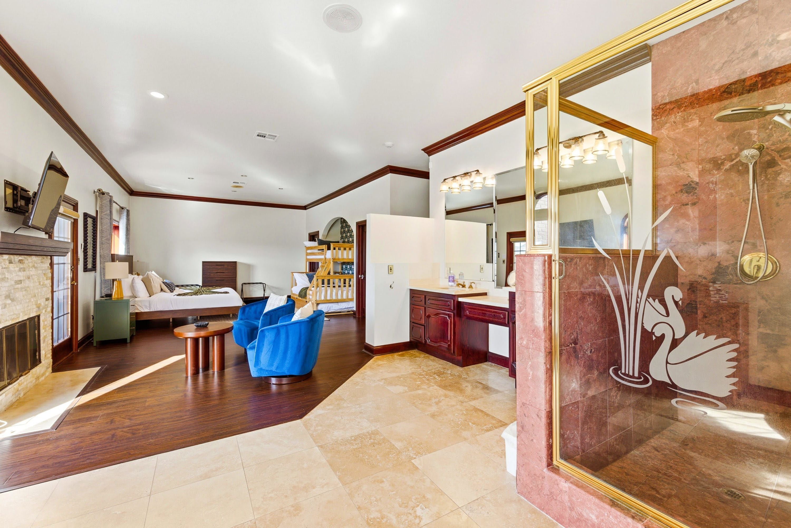 A spacious hotel room with a large bed, a sitting area with blue chairs, a bathroom with a large mirror and shower, and a dining area with a table and chairs.
