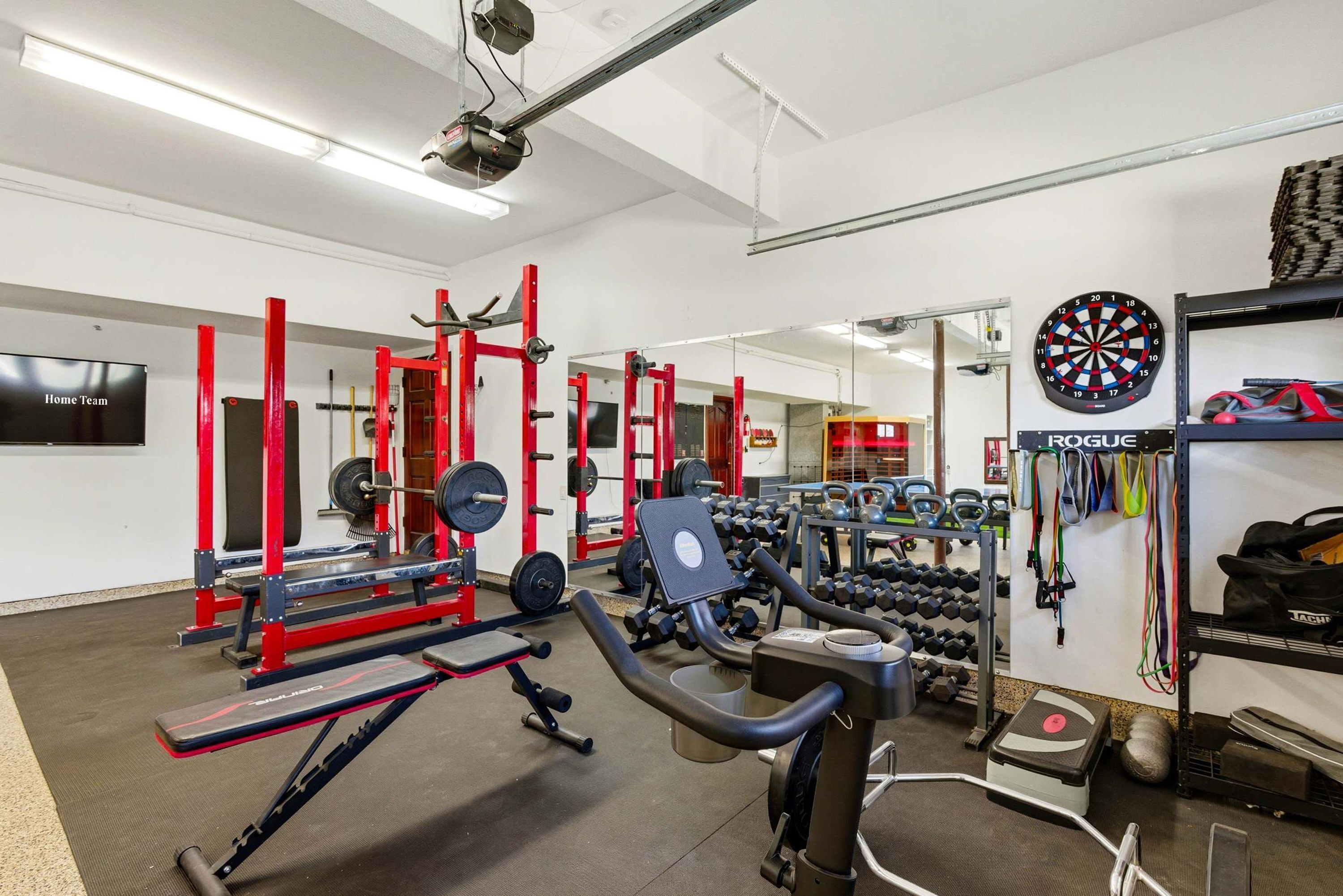 A gym with weightlifting equipment, cardio machines, and a dartboard.