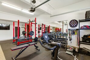 A gym with weightlifting equipment, cardio machines, and a dartboard. - Indoor Pool Spa - Gym - Sauna - Pickleball Court (Perris)