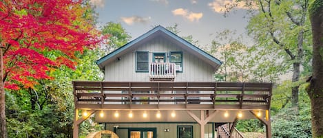 A two-story wooden house with a balcony, a hot tub, and a covered outdoor area with string lights.