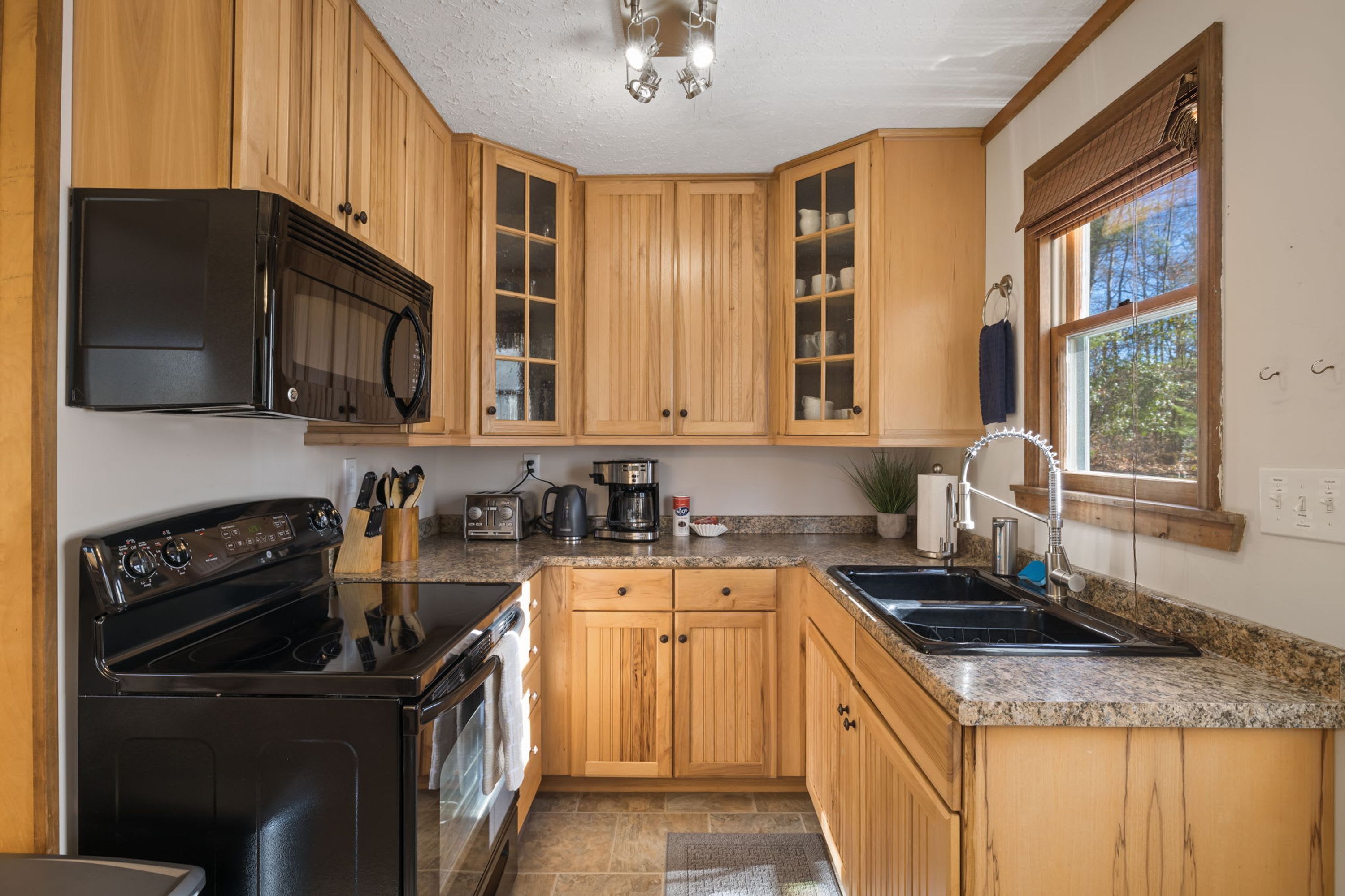 A kitchen with wooden cabinets, a black stove, a microwave, a coffee maker, and a sink.