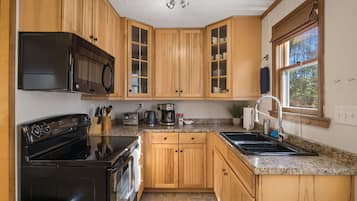 A kitchen with wooden cabinets, a black stove, a microwave, a coffee maker, and a sink.
