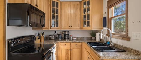 A kitchen with wooden cabinets, a black stove, a microwave, a coffee maker, and a sink.