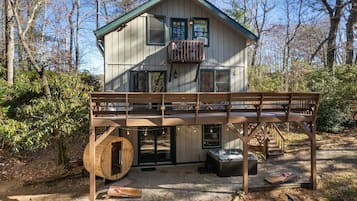 A cabin with a wooden deck, a hot tub, and a sauna.