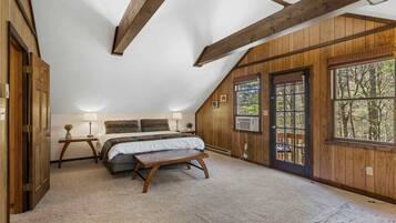 A bedroom with a bed, bedside tables, a bench, and large windows with a view of trees.