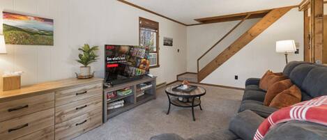 A cozy living room with a wooden TV stand, a sofa, and a staircase.