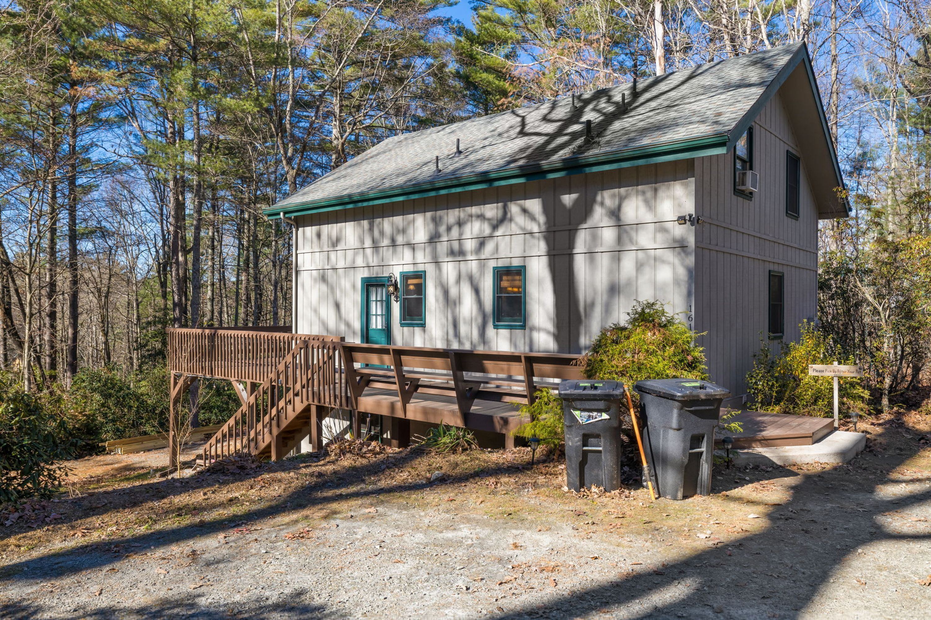 A small, single-story cabin with a wooden deck and a covered area, surrounded by trees.
