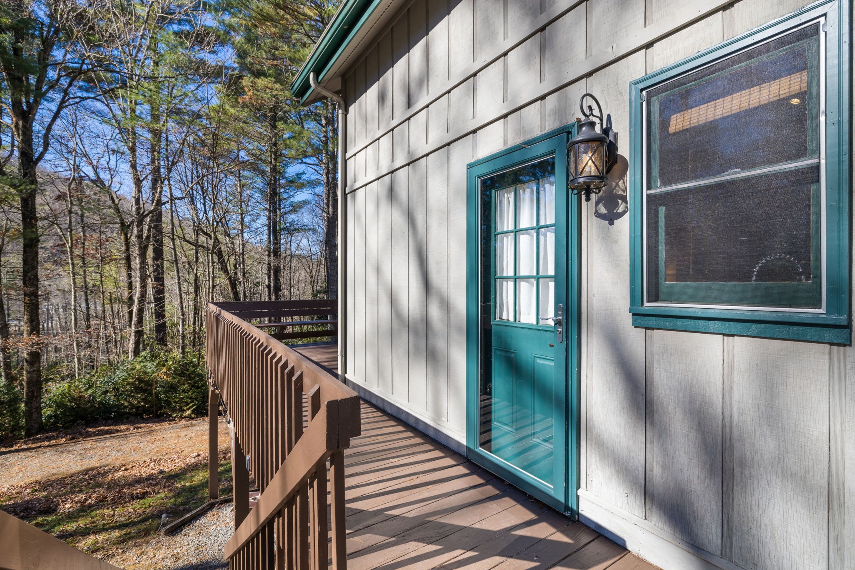 A wooden deck leading to a house with a green door and a window with a screen.